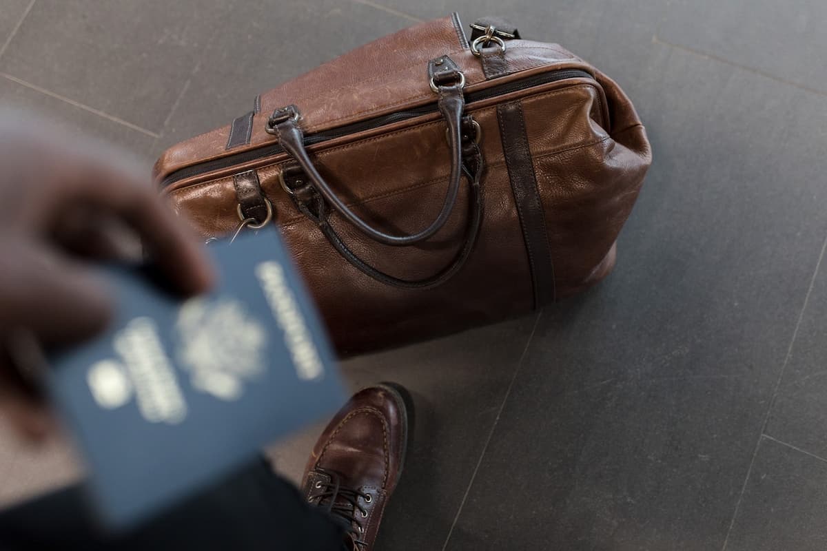 Imagem de uma mala no chão com uma pessoa segurando o passaporte