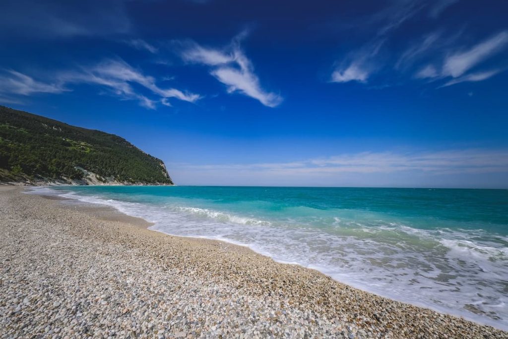 Imagem de uma faixa de areia com pequenas pedras de frente para o mar