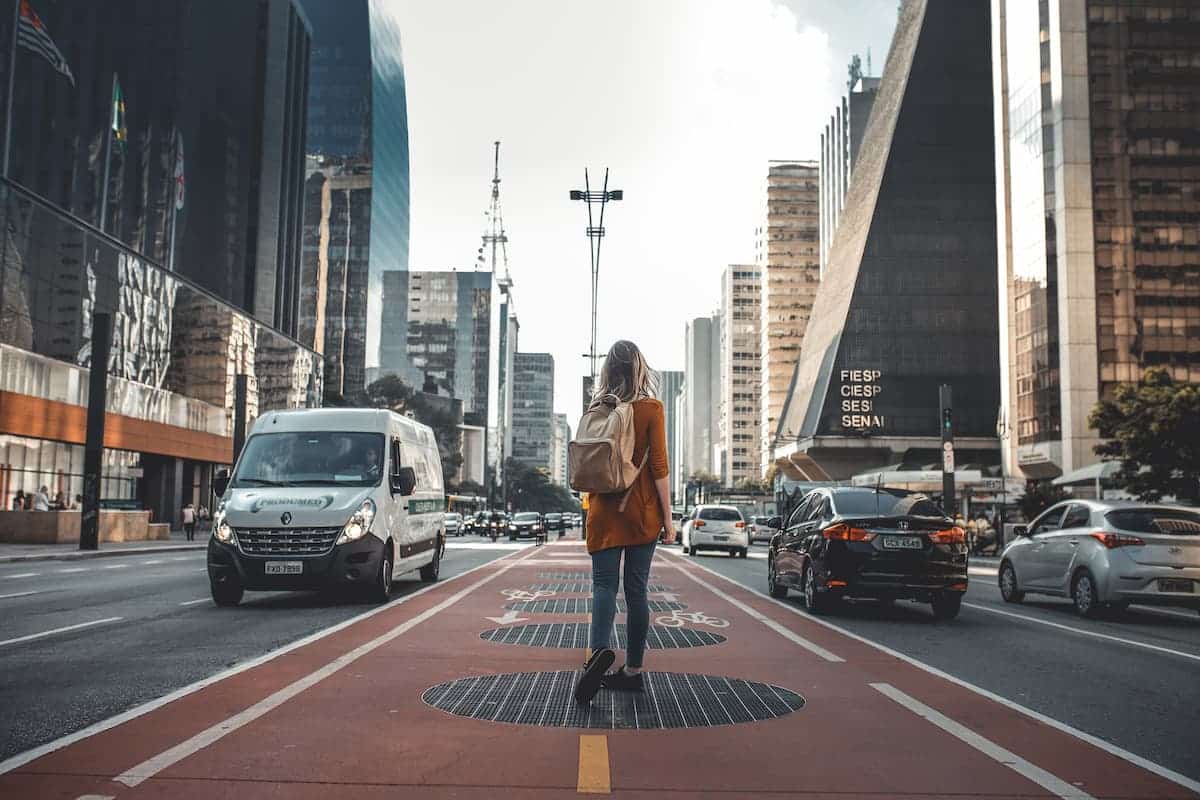 Mulher de mochila parada em uma avenida com veículos