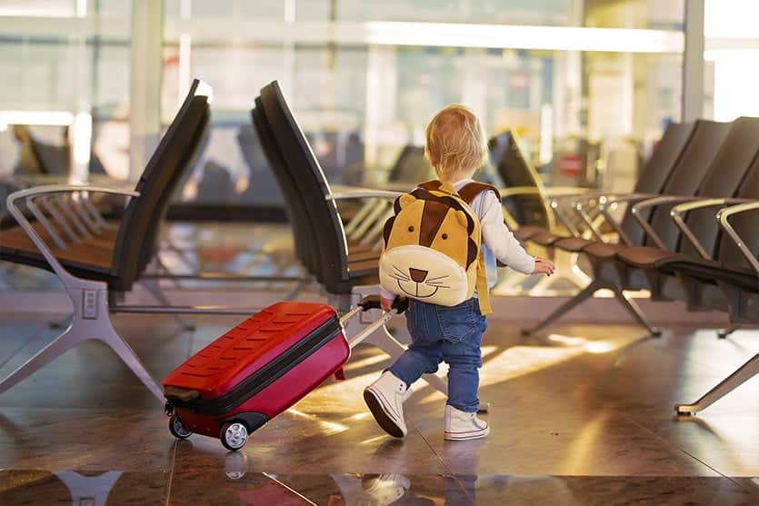 Criança pequena com mochila puxando uma mala de rodas em um aeroporto