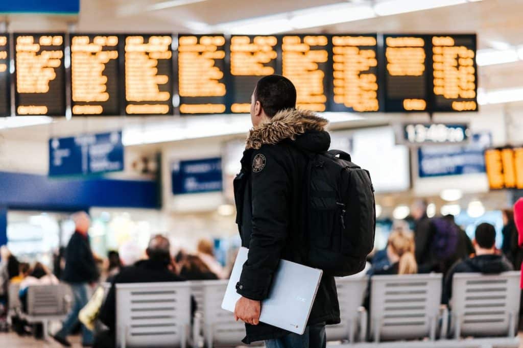 Homem com uma mochila nas costas e notebook nas mãos em um aeroporto