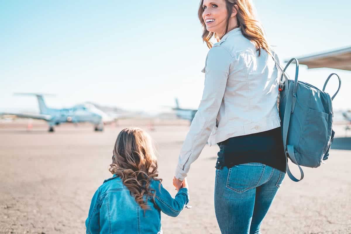Mulher adulta de mochila segurando a mão de uma criança para entrar no avião