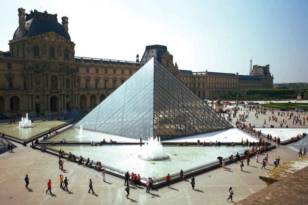Imagem de pessoas andando ao redor da Pirâmide do Louvre na França