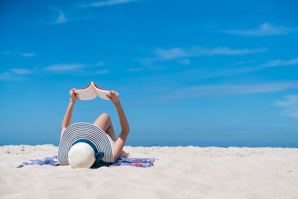 mulher de chapéu lendo livro na praia
