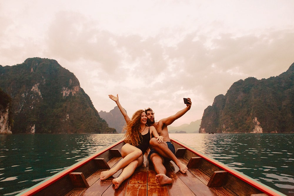 Casal posando para selfie com braços abertos em barco de madeira