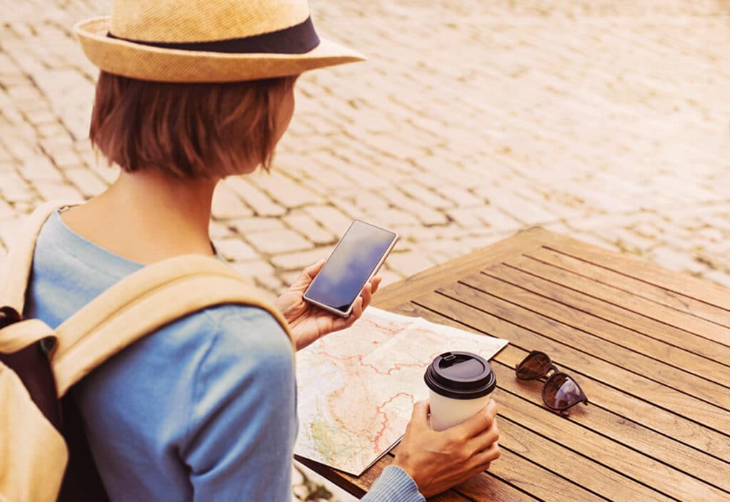 mulher de mochila com chapéu sentada procurando direções em um mapa tomando café