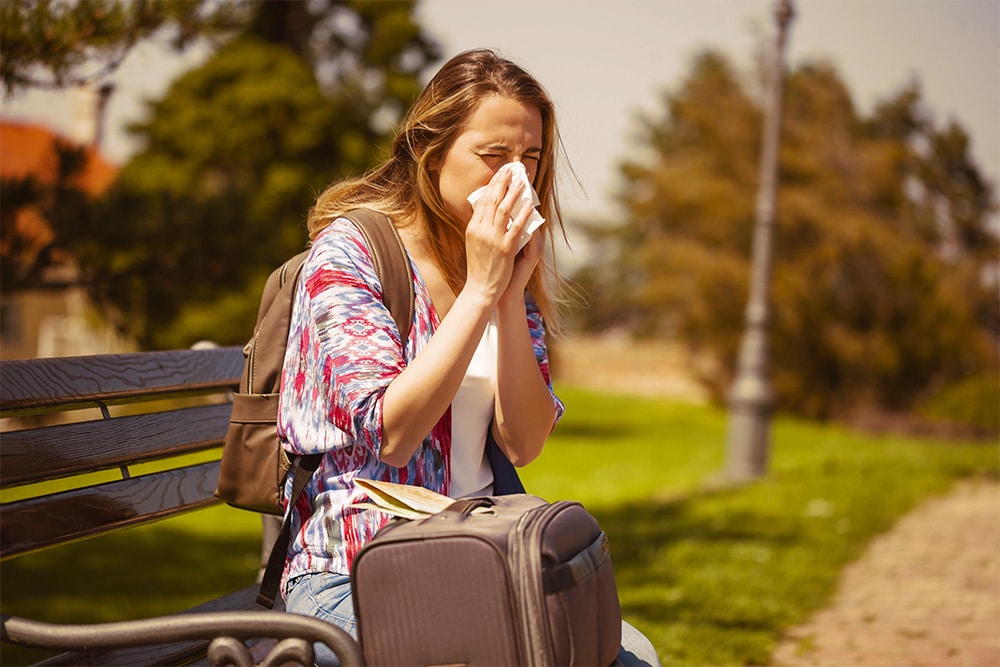 mulher com malas sentada em um banco limpando o nariz