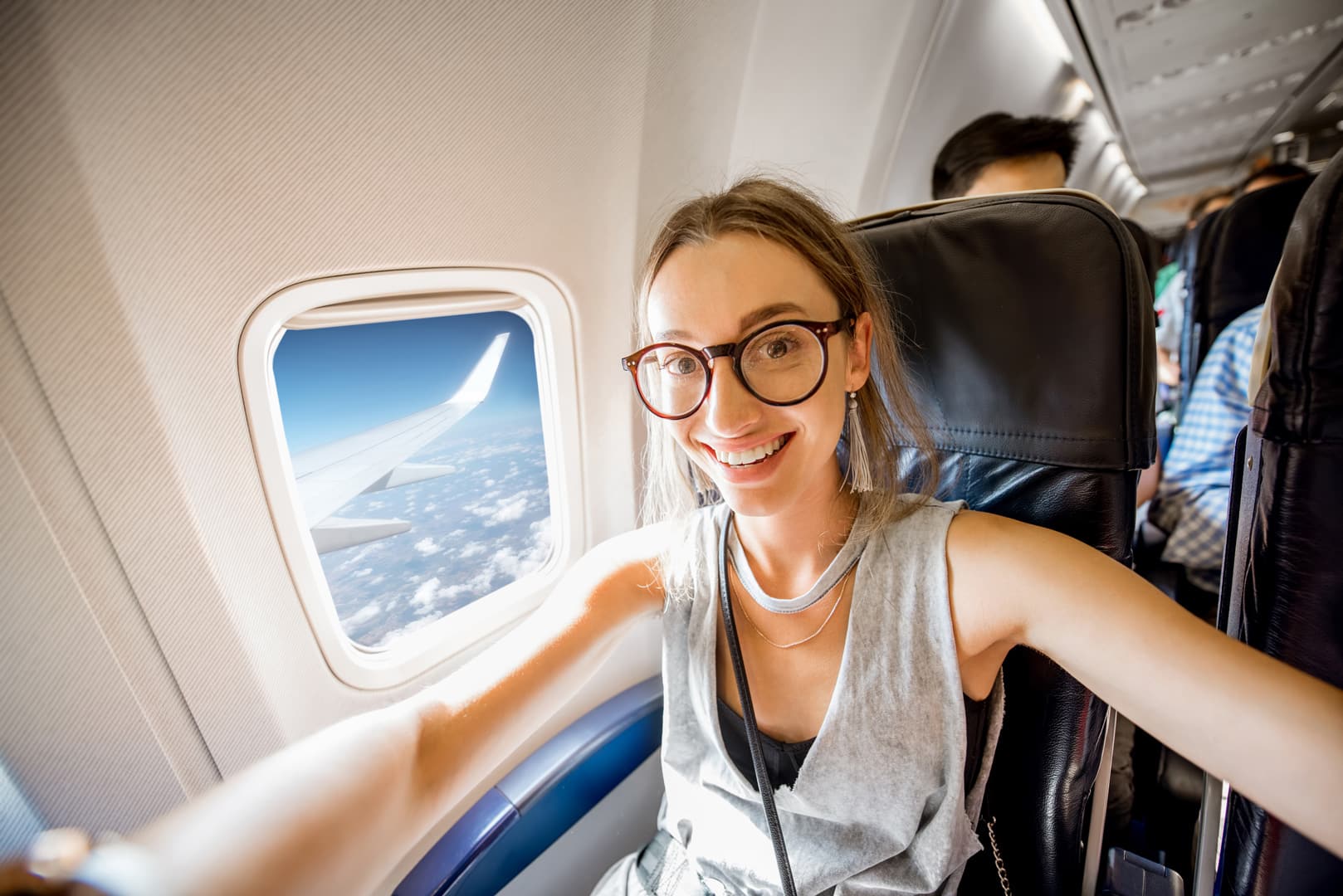 imagem de uma mulher sorrindo dentro de um avião sentada na poltrona da janela