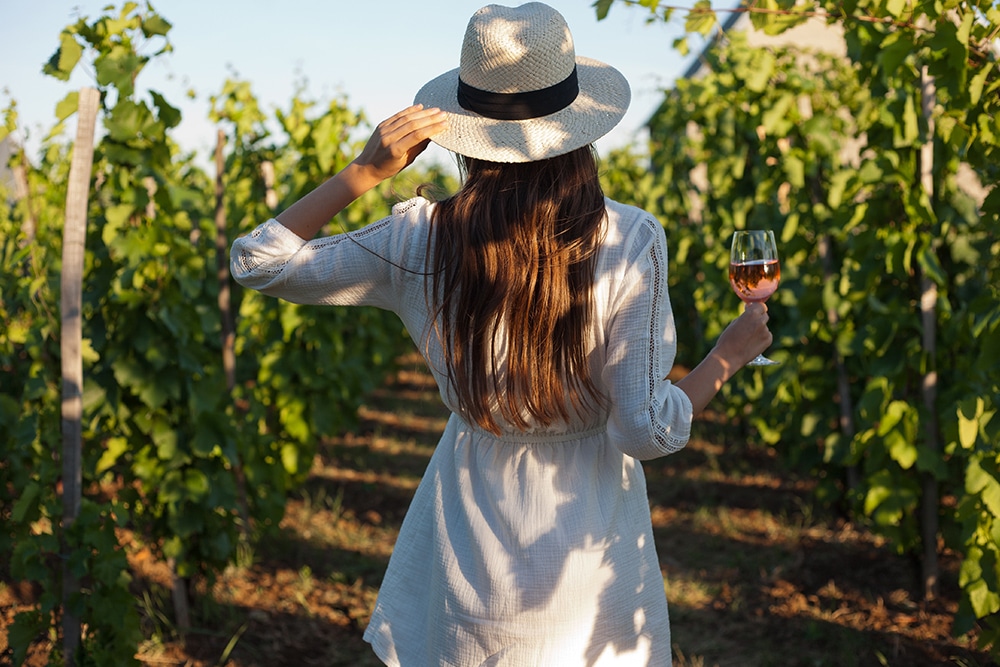 Mulher de costas segurando uma taça de vinho em uma vinha
