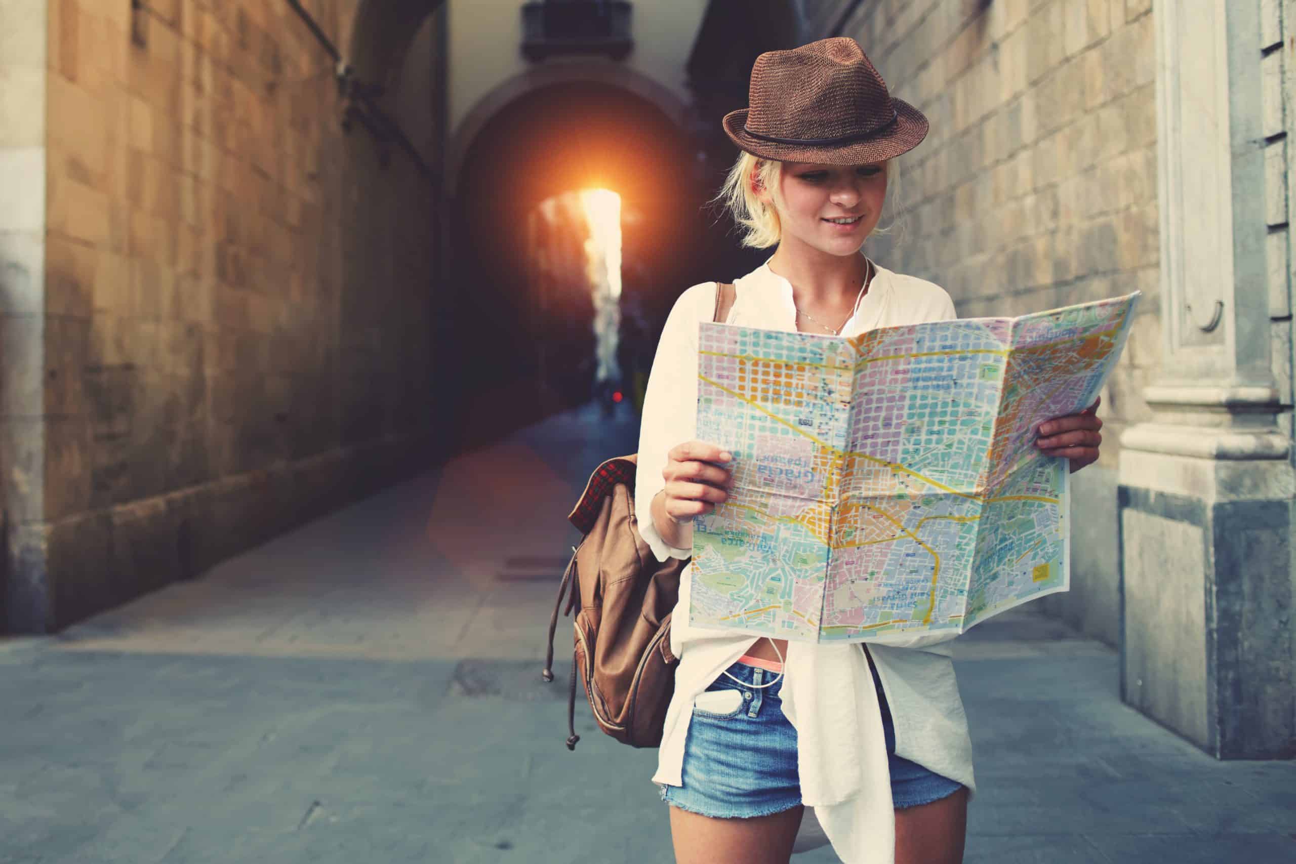 mulher com mochila e chapéu segurando um mapa, procurando direções