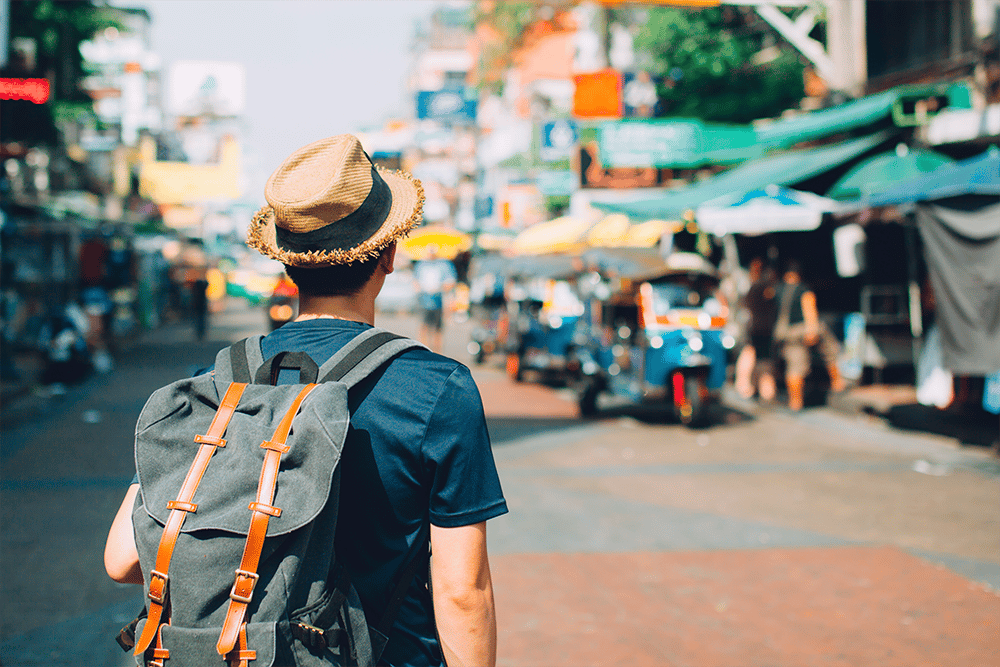 homem de mochila e chapéu em uma rua de um país estrangeiro