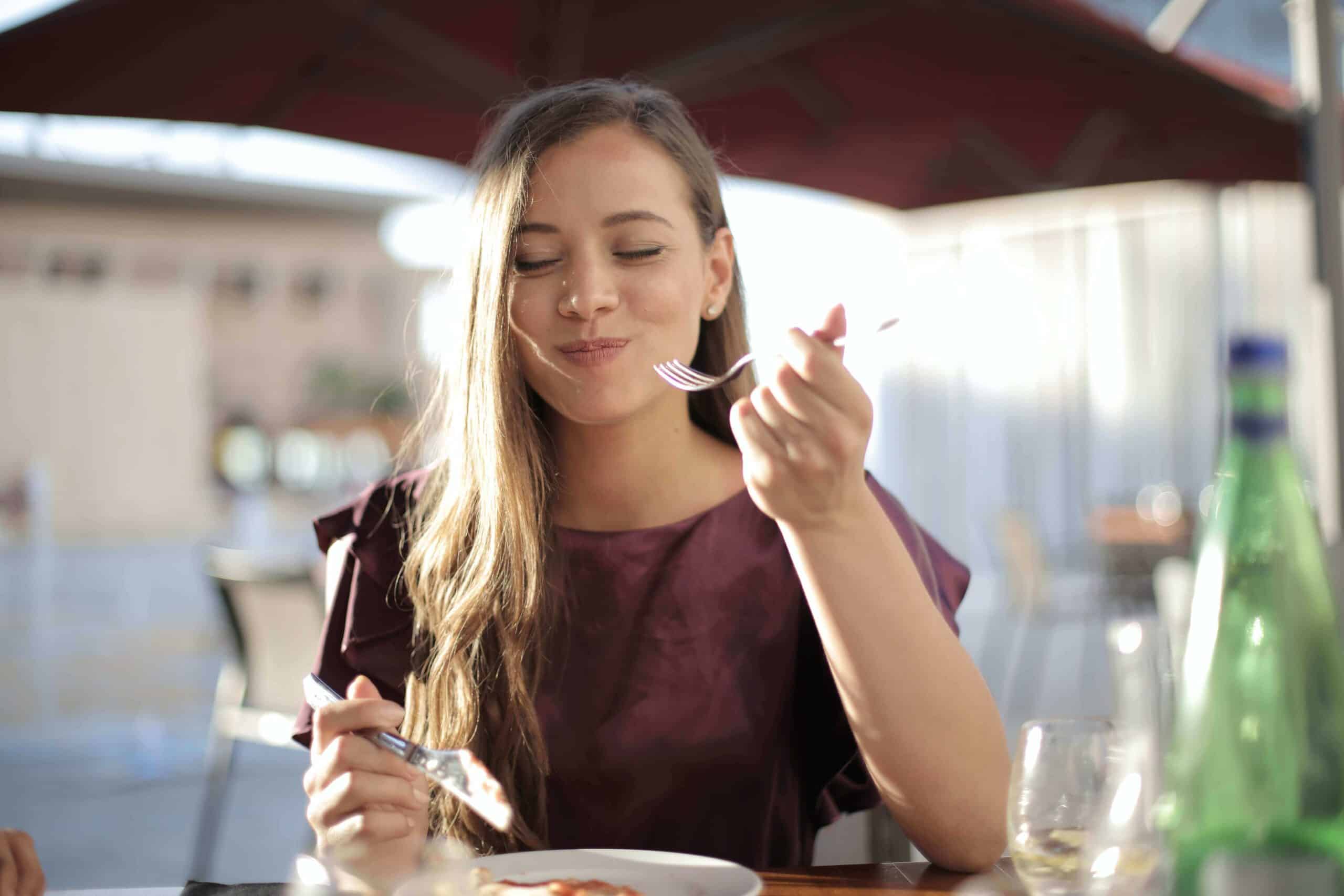 Mulher comendo e sorrindo durante uma viagem gastronômica.