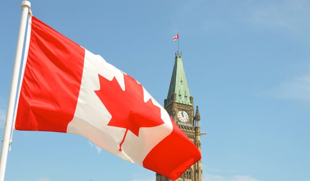 Bandeira do Canadá com torre de relógio ao fundo com bandeira menor no topo