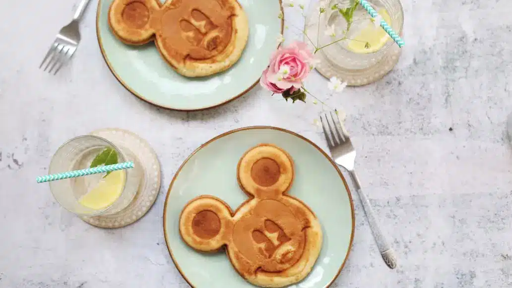 Dois pratos com panquecas no formato da cara do Mickey com garfos ao lado e copos