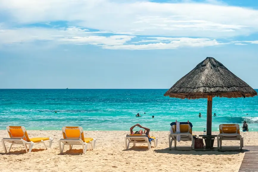 Foto da praia de Cancun, no México, com espreguiçadeiras na areia e sombreiro de palha