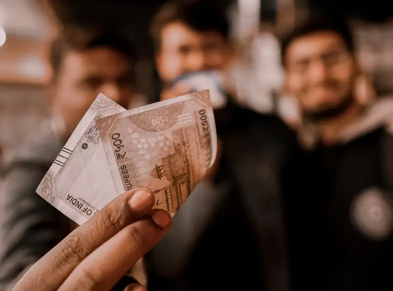 3 homens ao fundo embaçados mostrando uma nota de dinheiro indiano a frente