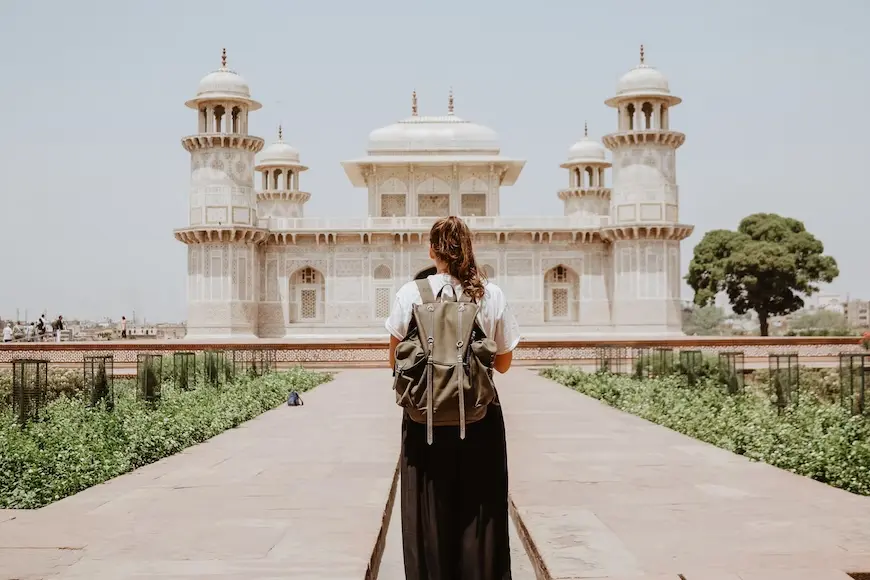 Mulher parada em pé com mochila nas costas em frente a um monumento da Índia