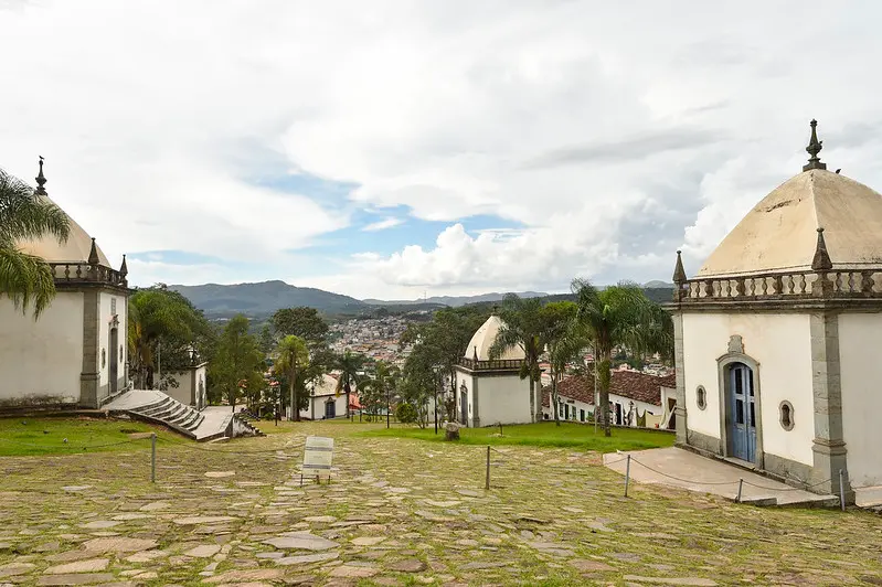 Prédios do estilo colonial em praça com coqueiros com cidade ao fundo entre montanhas