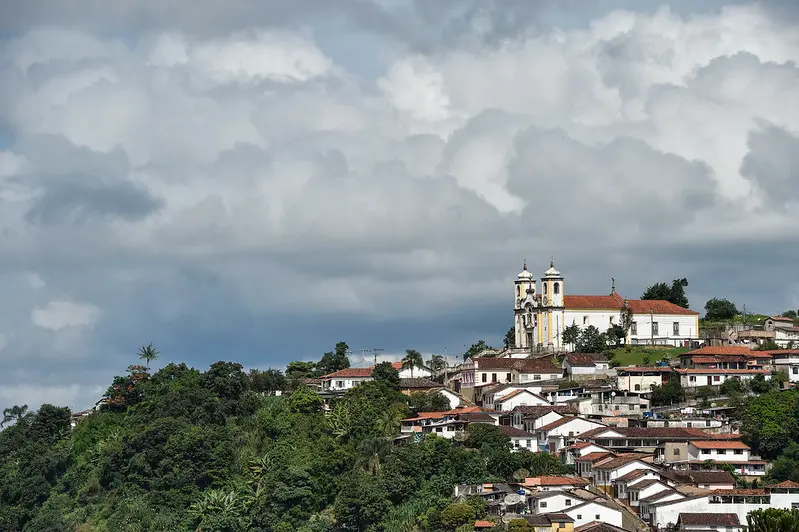 Cidade de Ouro Preto com igreja no topo, mata ao lado e núvens ao fundo