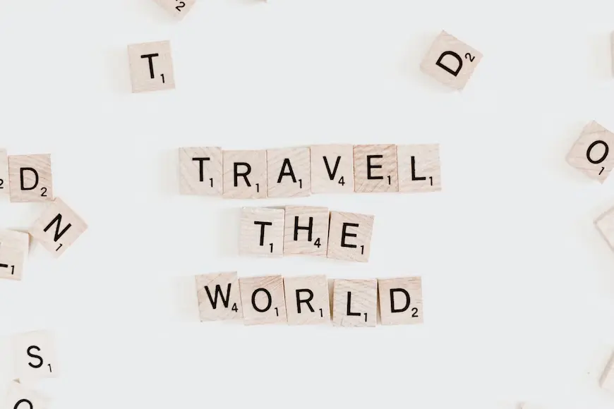 Peças de madeira cada uma com uma letra e um número pequeno embaixo, representando a pontuação do respectivo jogo de montar palavras, com as letras do meio escrito "Travel the World"