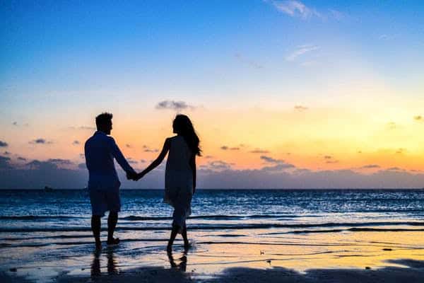 Casal de mãos dadas na beira da praia ao pôr do sol