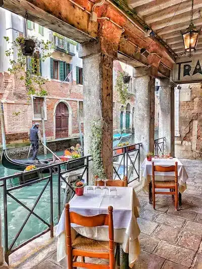 Mesas em um terraço a beira de um canal com gôndola em Veneza na Itália