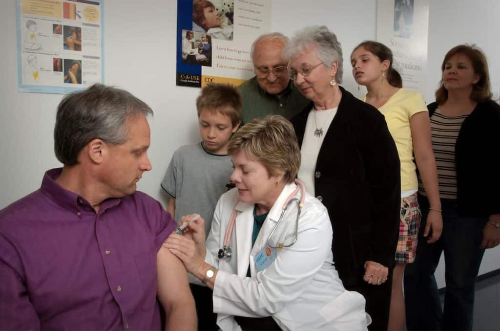 Grupo de pessoas vendo um homem ser vacinado