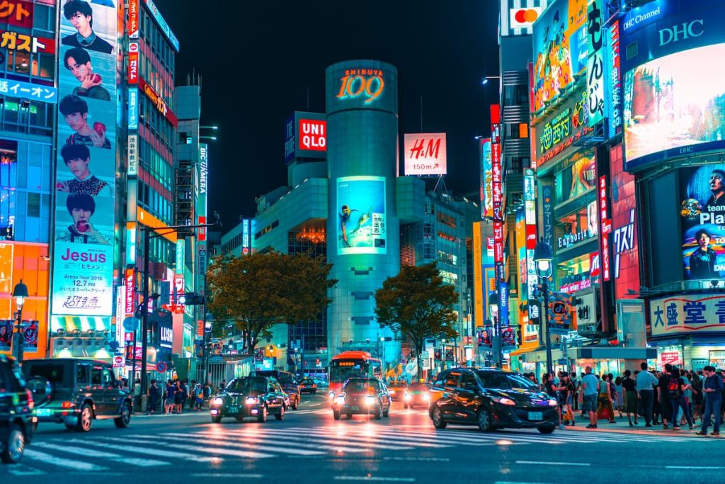 Uma rua cheia de letreiros, pessoas e carros no Japão